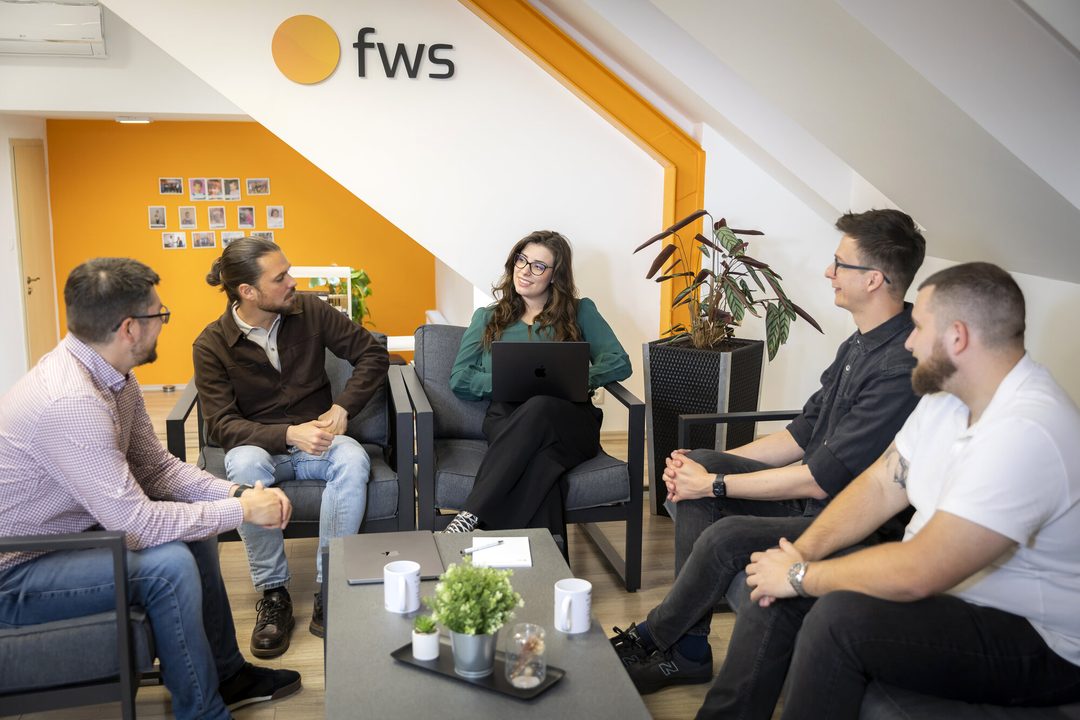 Az fws csapata kötetlen megbeszélésen az irodai társalgóban, a falon az fws logó