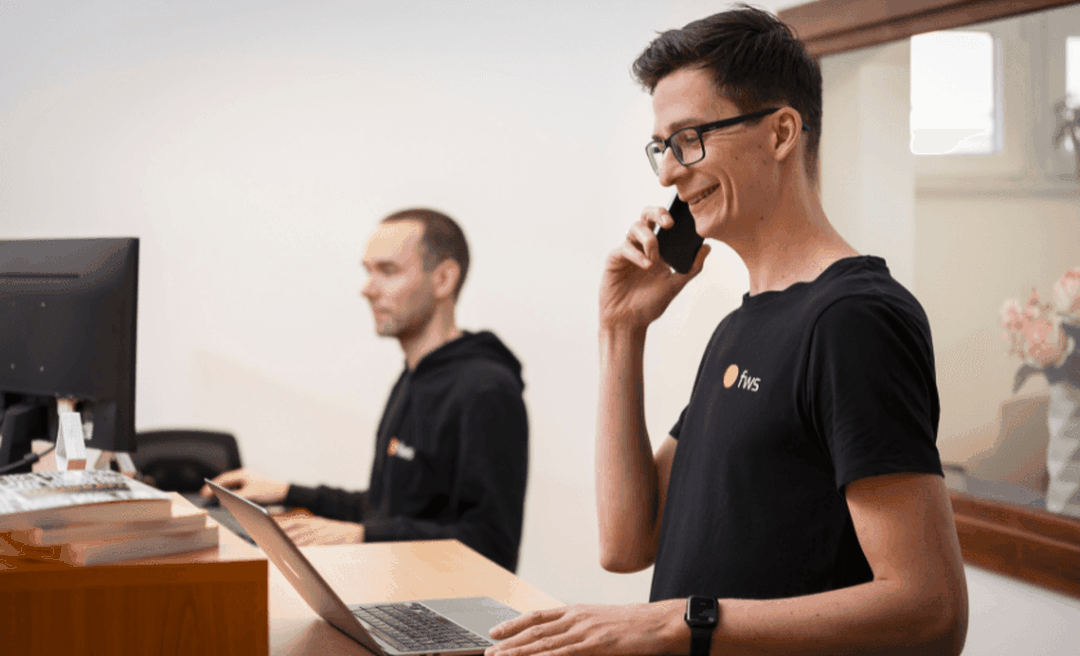 Az fws projektmenedzsere mosolyogva telefonál a pultnál, mögötte egy kolléga számítógépen dolgozik