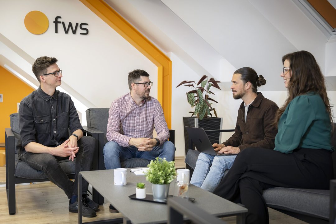 Az fws csapatának négy tagja beszélget az iroda társalgójában, a falon az fws logó