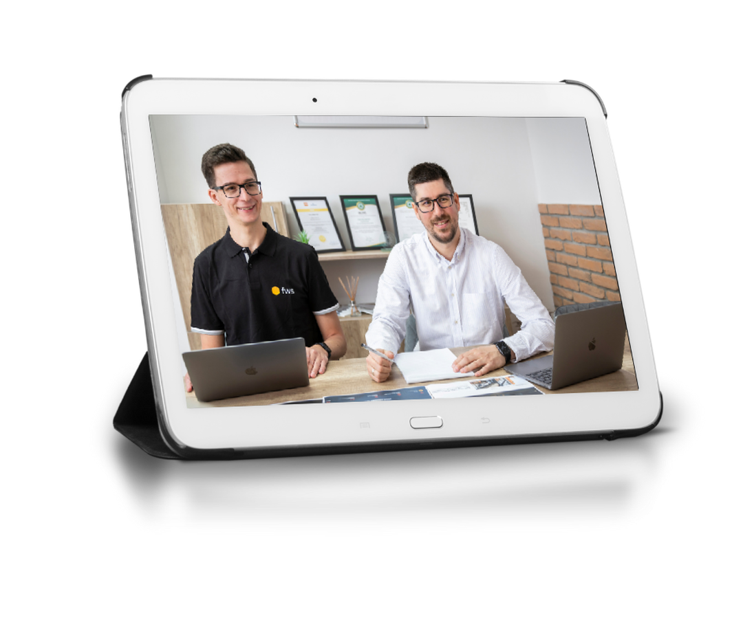 Tablet kijelzőjén két mosolygó fws-munkatárs laptopok mögött ül, online konzultáció közben