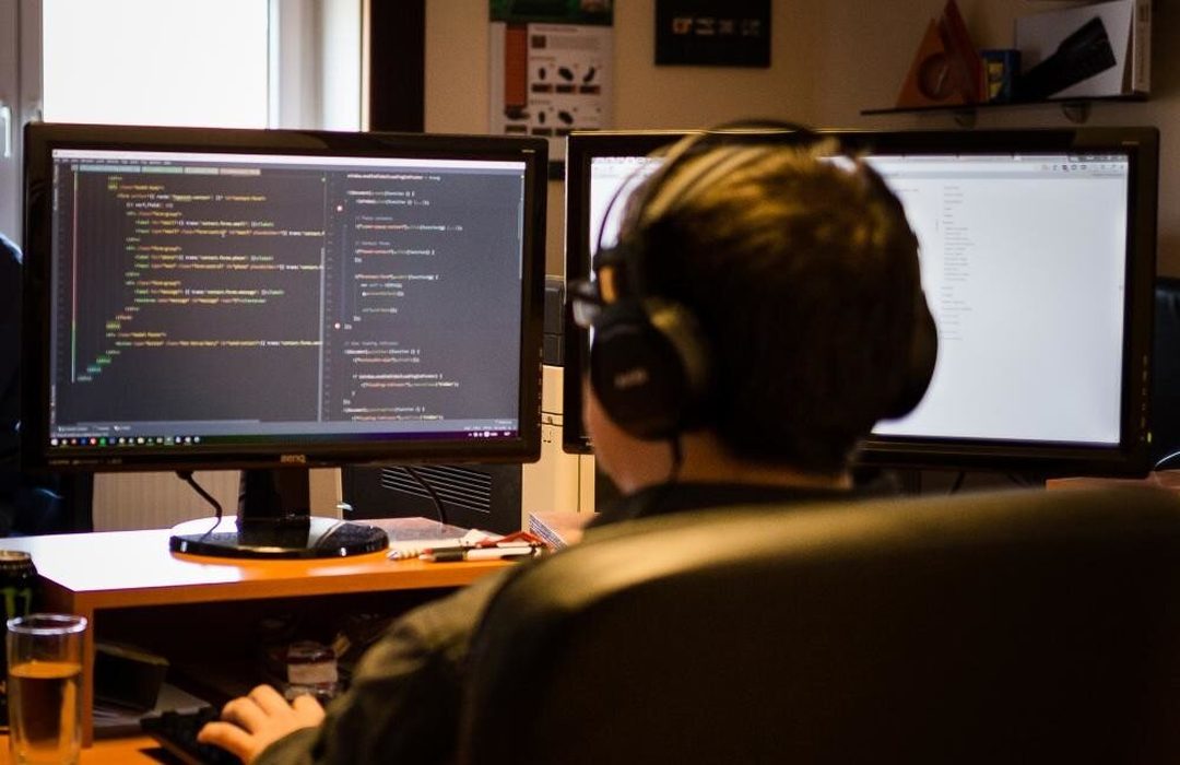 Fejhallgatós fejlesztő két monitor előtt dolgozik, a bal oldali képernyőn programkód látszik