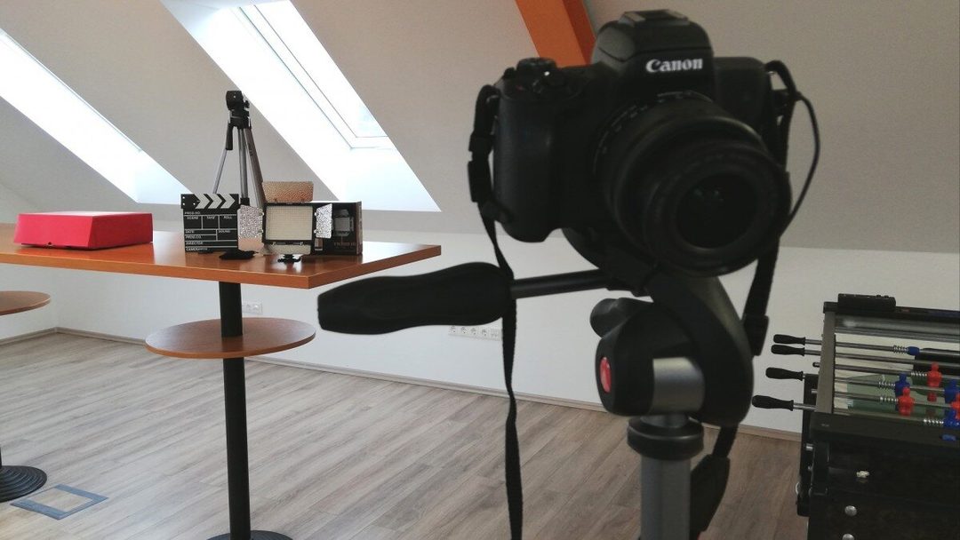 Állványra szerelt Canon fényképezőgép az irodában, a háttérben csapó, videólámpa és kisebb állvány az asztalon