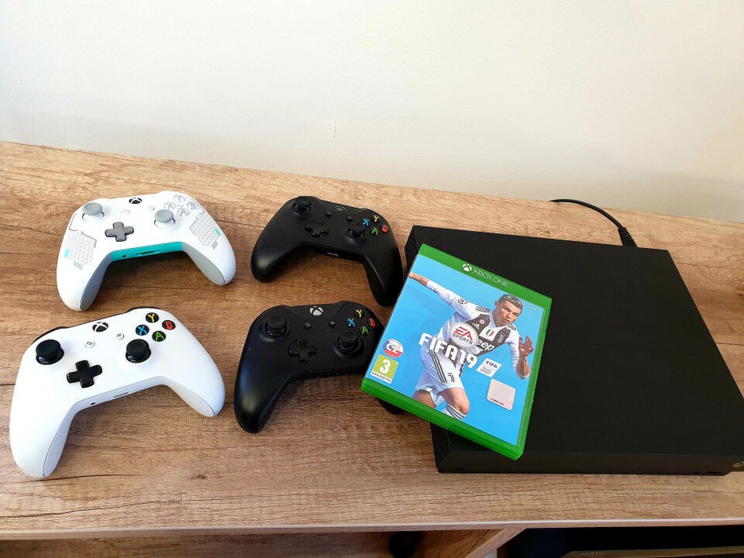 Xbox One konzol, négy kontroller és egy FIFA 19 játéklemez egy asztalon