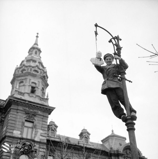 Rákosi porcelán szobrát „akasztja” egy fiatal fiú a győri Városháza tér egyik póznáján kapaszkodva november 1-jén vagy 2-án. 