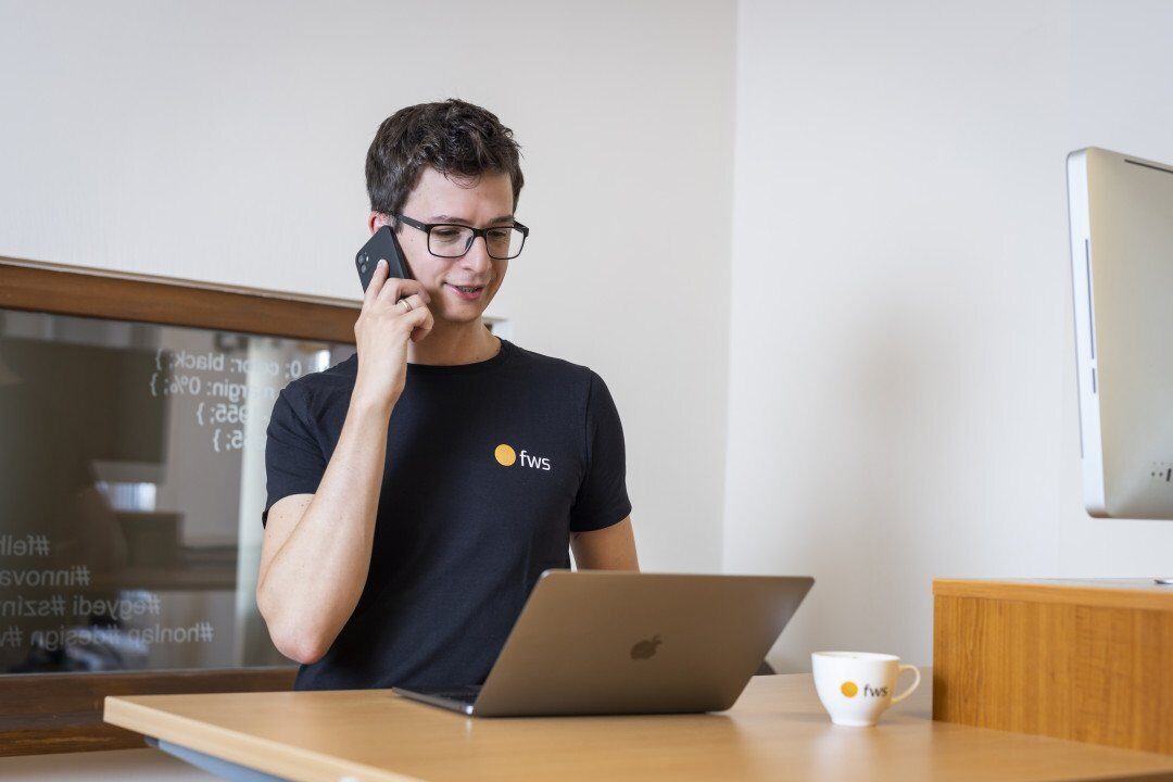 Peti, az fws projektmenedzsere telefonál egy laptop előtt az irodában