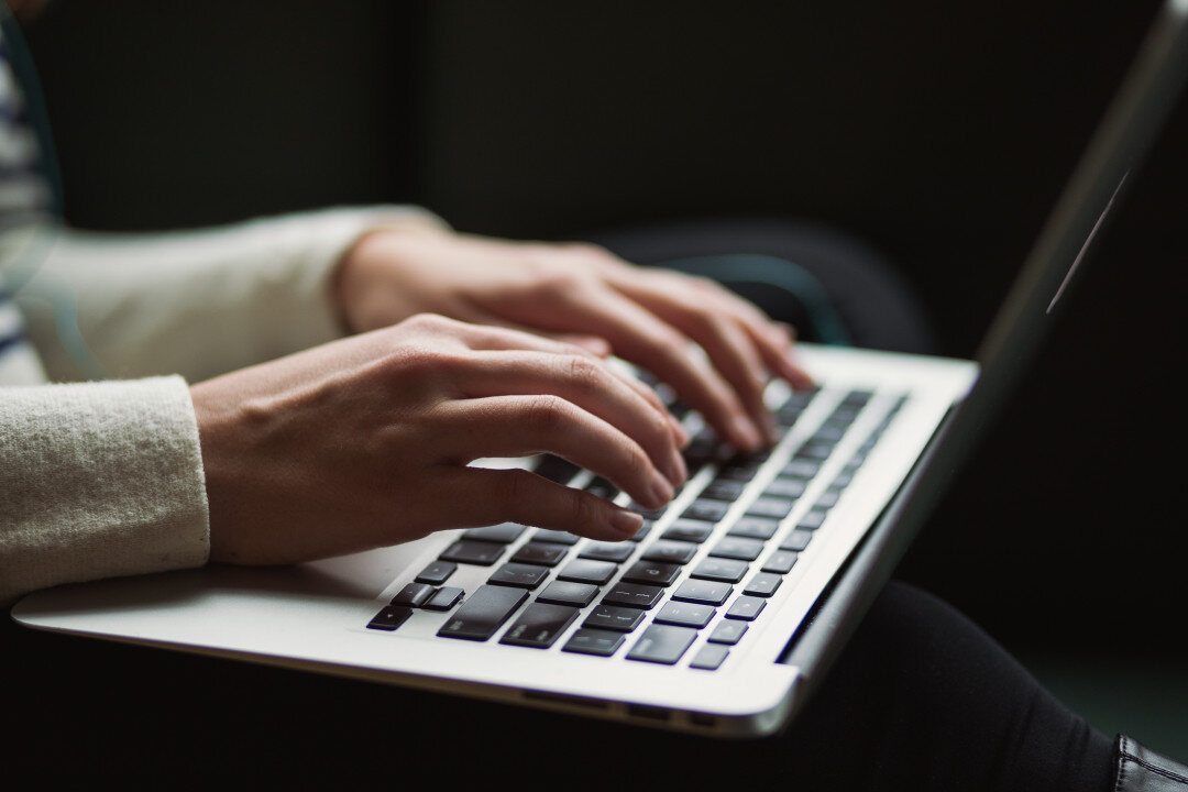 Laptopon gépelő kezek közelről, sötét háttér előtt
